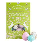 Cartwright & Butler Dragierte Mini Schokoladenostereier mit Haselnuss, 200 g: Eine grüne Box mit Mini-Ostereiern. Drei pastellfarbene, gesprenkelte Eier liegen vor der Schachtel.